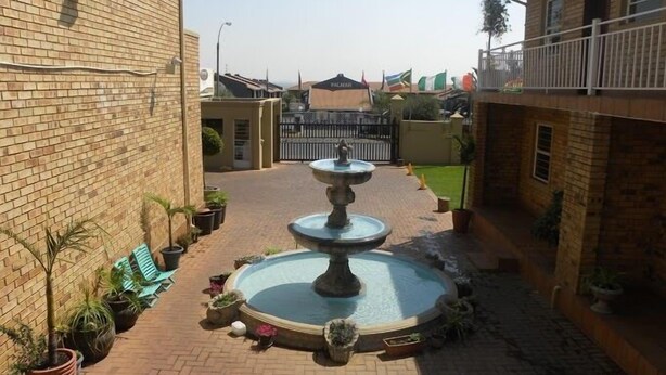 A courtyard with a central fountain, potted plants, and a brick pathway. - Croydon hotel (Kempton Park)