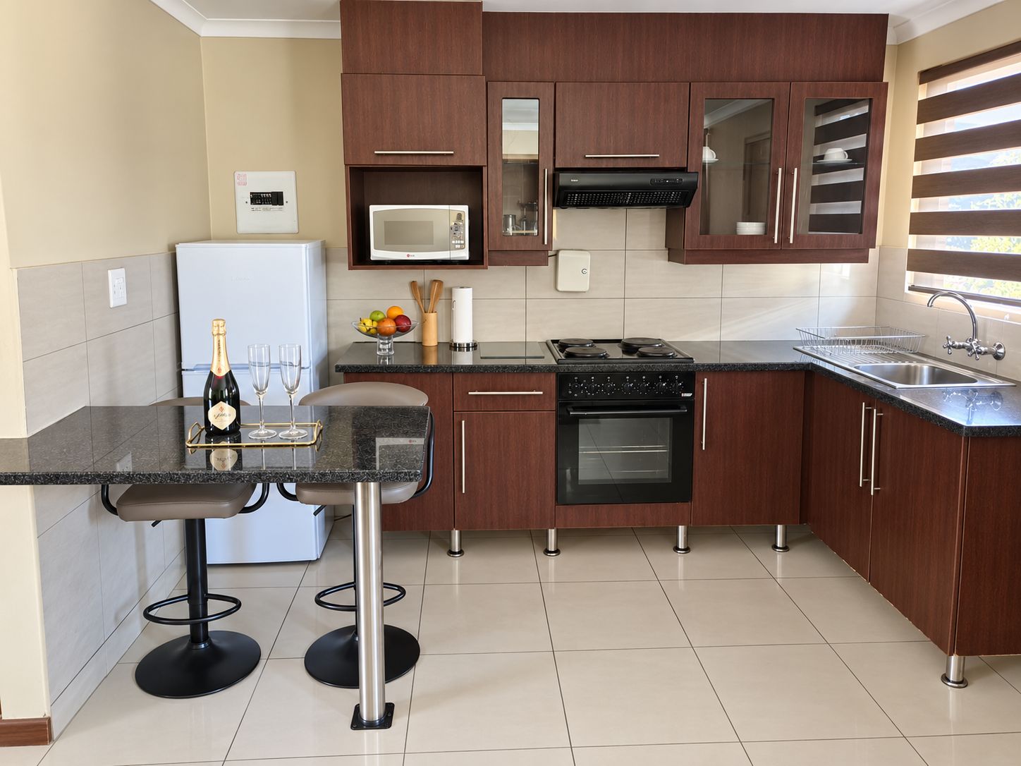 Una cocina moderna con armarios de madera oscura, encimera negra, microondas integrado, estufa y refrigerador.