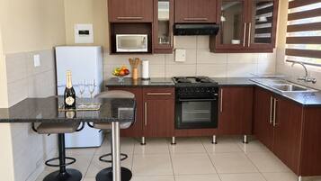 Una cocina moderna con armarios de madera oscura, encimera negra, microondas integrado, estufa y refrigerador.