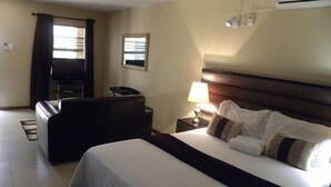 A hotel room with a bed, a desk, a chair, a lamp, and an air conditioner. - Croydon hotel (Kempton Park)