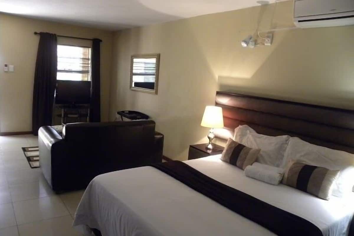 Een hotelkamer met een bed, een bureau, een stoel, een lamp en een airconditioner.