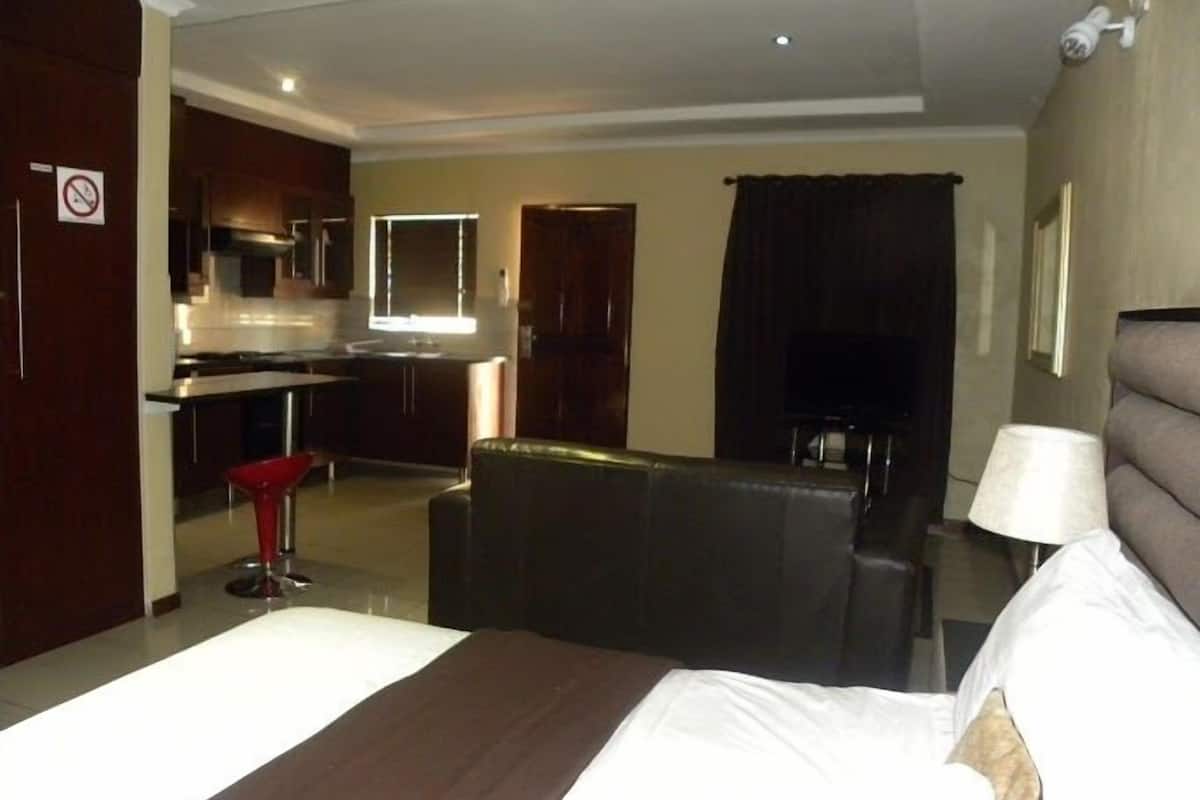 Een hotelkamer met een bed, een kleine zithoek, een eethoek met een tafel en stoelen, en een keuken op de achtergrond.