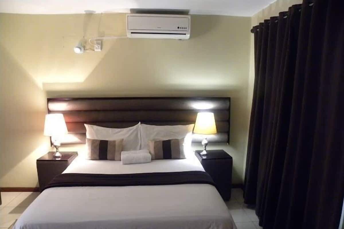 Een hotelkamer met een bed, twee bedlampen, een wandairconditioner en een gordijn.