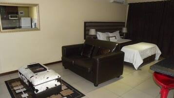 Habitación de hotel con cama, sofá, una mesita, un taburete rojo y una maleta.