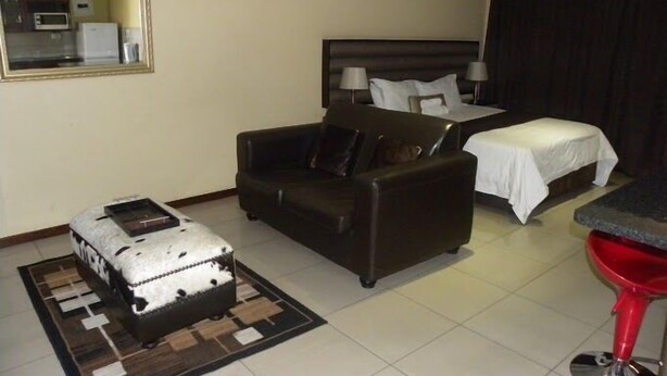 Habitación de hotel con cama, sofá, una mesita, un taburete rojo y una maleta.