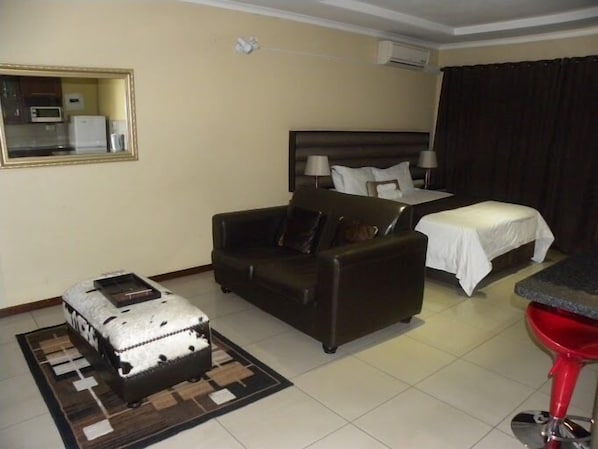 A hotel room with a bed, a sofa, a small table, a red bar stool, and a suitcase.