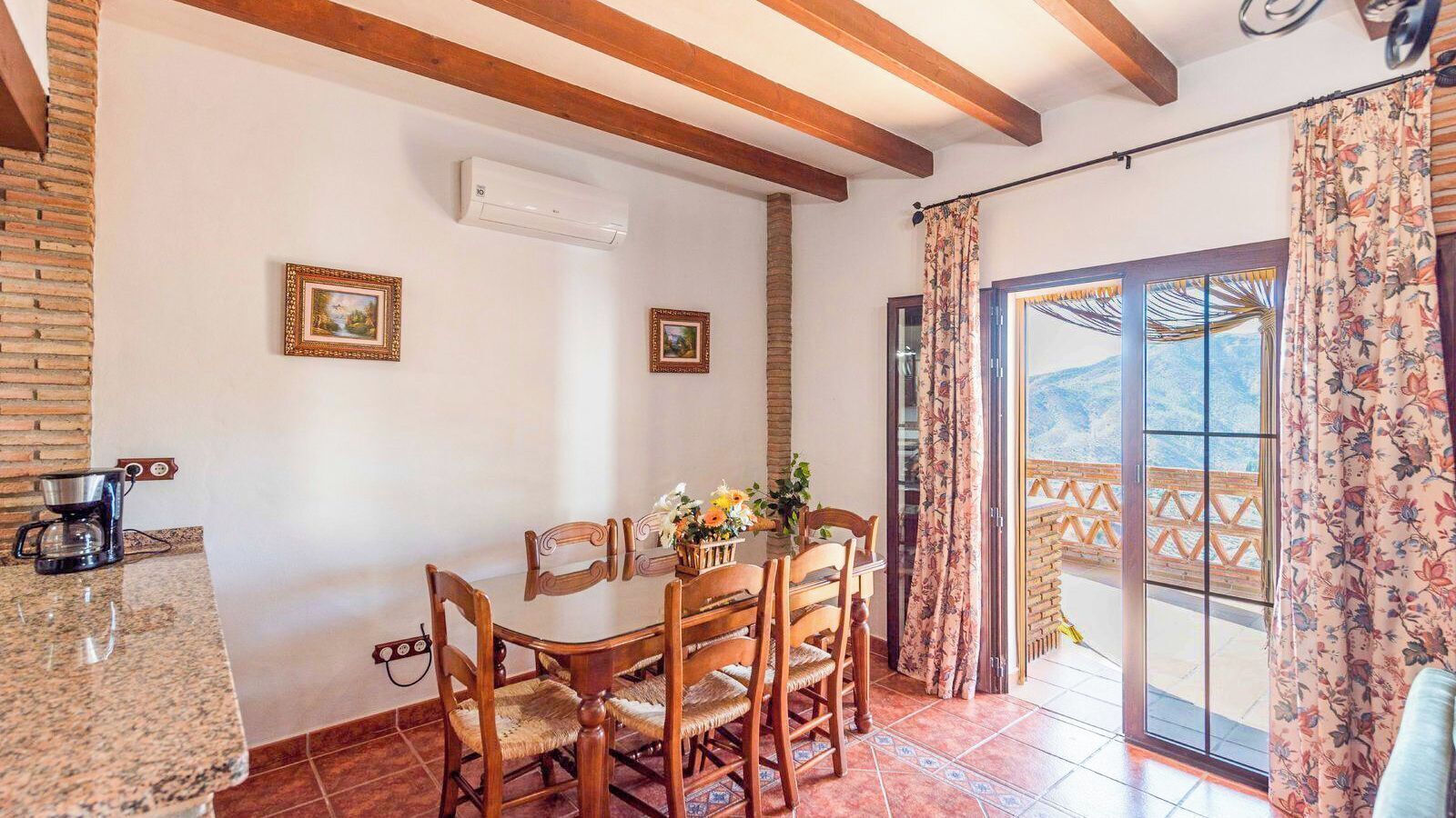 A dining area with a table and chairs, an air conditioning unit, and a view through a glass door.