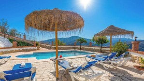 A poolside area with lounge chairs, a small table, and a decorative umbrella. - El Algarrobo de Alora Álora by Ruralidays (Málaga)