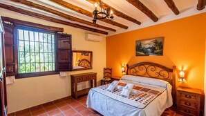 Een slaapkamer met een bed, een dressoir, een bureau en een raam met uitzicht op groen.