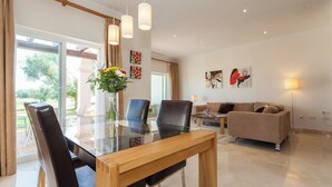 Ein modernes Wohnzimmer mit einem Glastisch, Ledersesseln, einem beigefarbenen Sofa und Kunstwerken an den Wänden.