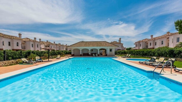 Ein Swimmingpool mit Liegestühlen und ein Gebäude mit einem Ziegeldach im Hintergrund.