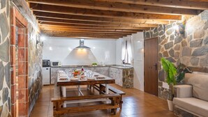 Una cocina rústica con pared de piedra, vigas de madera y una mesa para cuatro comensales.