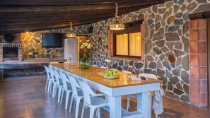 Un coin repas agrémenté d’un mur en pierre, d’un plafond en bois et d’un téléviseur fixé au mur.