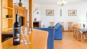 Ein Holztisch mit einer Flasche und Gläsern, ein blaues Sofa und ein Essbereich mit Stühlen und Tisch.