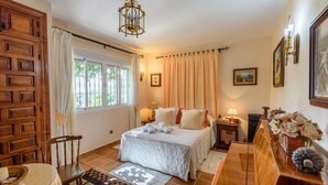 Un dormitorio bien iluminado con una cama grande, un armario de madera, un escritorio con lámpara y vistas al exterior a través de la ventana.