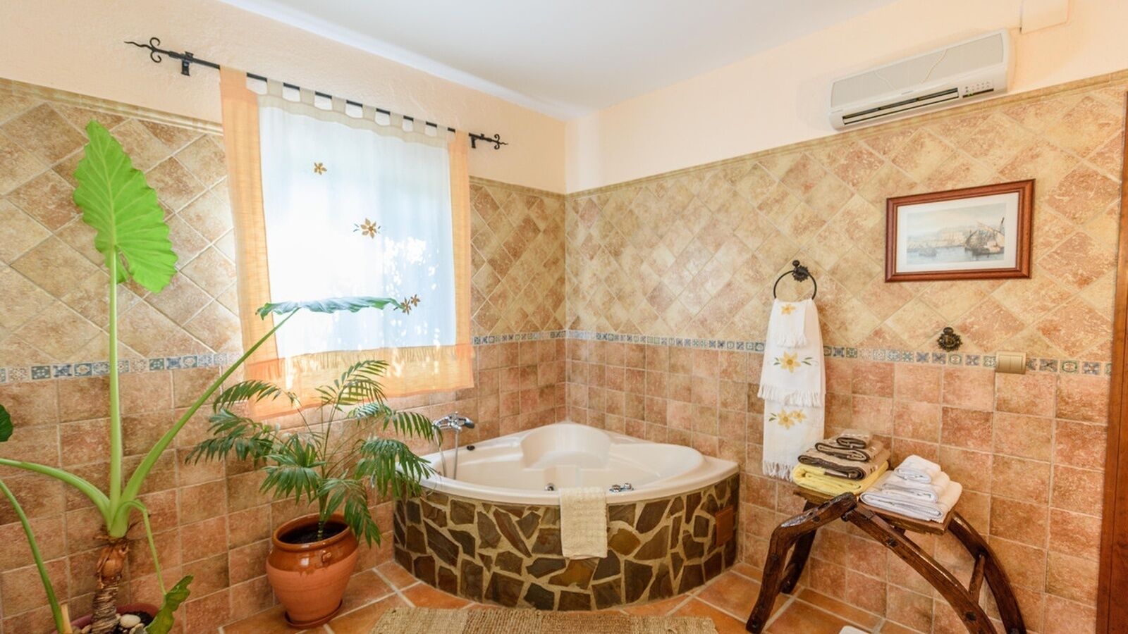 A bathroom with a stone bathtub, a potted plant, a towel rack, and a framed picture on the wall.