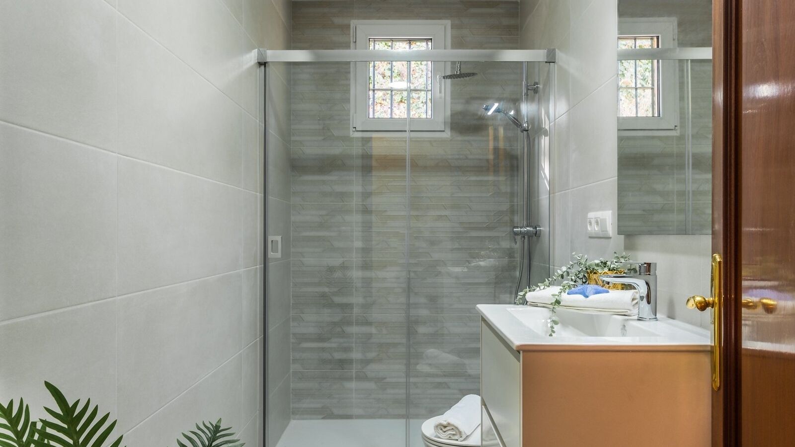 A modern bathroom with a glass-enclosed shower, a white sink with a gold faucet, and a large mirror.