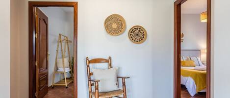 A room with a wooden chair, a ladder, and two wall decorations.