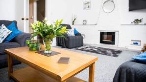 Una sala de estar moderna con una mesa de centro de madera, un florero con flores, un sofá gris con cojines azules y una chimenea.
