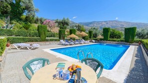 A pool area with a table and chairs, surrounded by neatly trimmed hedges and a view of the mountains. - Casa Delia Órgiva by Ruralidays (Granada)