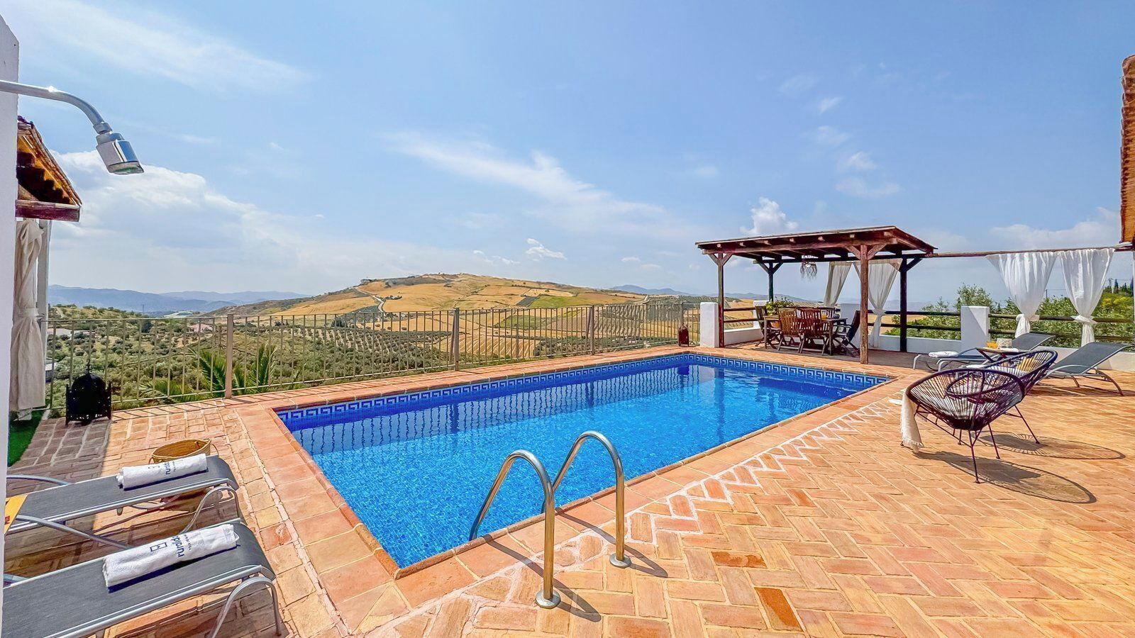 Une piscine avec vue sur la campagne, un espace salon couvert et des chaises longues.