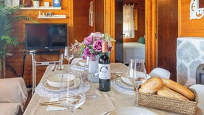 A wooden cabin interior with a dining table set for two, a bottle of wine, and a basket of bread. - Hornillos Alozaina by Ruralidays (Málaga)