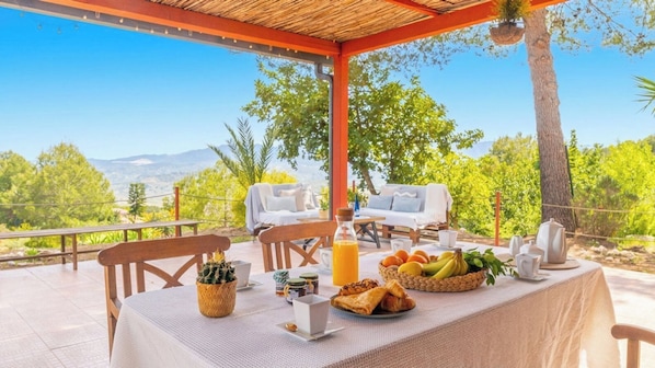An outdoor dining area with a table set for breakfast, chairs, and a view of the landscape.