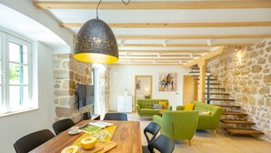 A modern living room with a wooden dining table, green sofas, and a stone wall. - Hedera Estate, Villa Hedera IV (Dubrovnik)