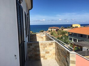 A balcony with a stone wall and a view of the sea and neighboring buildings. - Appartamenti Pigafetta (Valledoria)