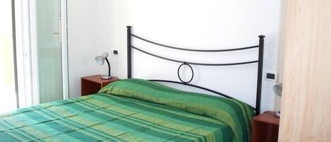 A single bed with a green striped bedspread, a bedside table with a lamp, and a small picture on the wall.
