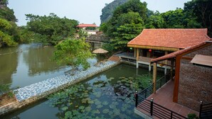 A traditional building with a tiled roof and a wooden balcony overlooking a pond with lily pads. - Ninh Binh Valle Montana homestay (Hoa Lu)