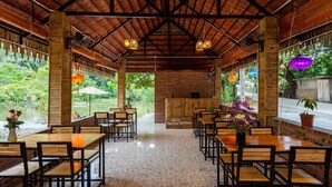 A restaurant with wooden tables and chairs, a brick wall, and a view of greenery. - Ninh Binh Valle Montana homestay (Hoa Lu)