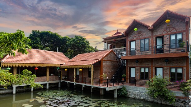 A traditional building with a brick facade, wooden balconies, and a waterway with lily pads. - Ninh Binh Valle Montana homestay (Hoa Lu)