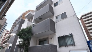 Un immeuble résidentiel à plusieurs étages, doté de balcons, avec un arbre devant et un ciel dégagé.