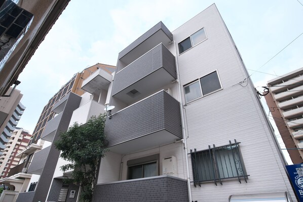 A multi-story residential building with balconies, a tree in front, and a clear sky.