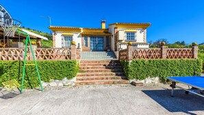 A two-story house with a staircase leading to the entrance, a tennis court, and a green swing set. - Villa Jiminez - A104 Coín by Ruralidays (Málaga)