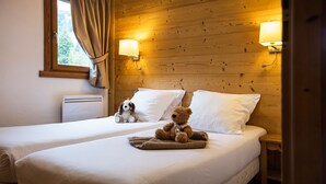 Een hotelkamer met twee bedden, een raam met gordijnen, een wandlamp en een teddybeer op het bed.
