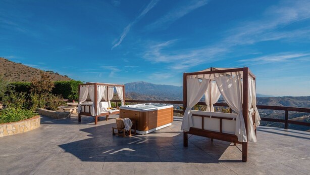 Une terrasse sur le toit, dotée de deux lits à baldaquin en bois et d’un jacuzzi, offrant une vue sur un paysage montagneux.