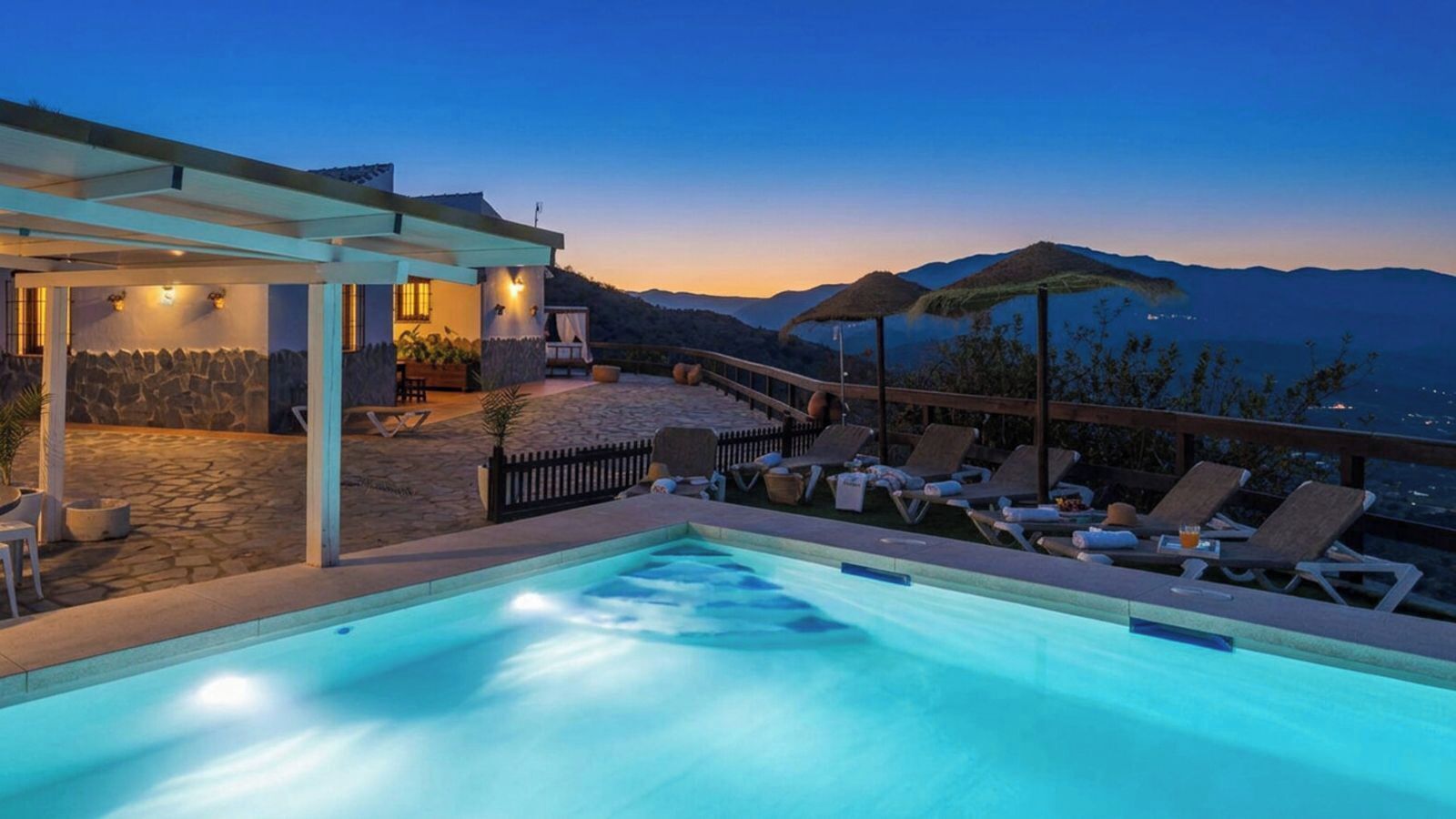 Una piscina con sillas de descanso y una zona de estar cubierta, con vistas a un paisaje montañoso.