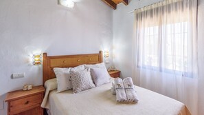 A neatly made bed with white linens and patterned pillows, a wooden headboard, and a nightstand with a lamp.