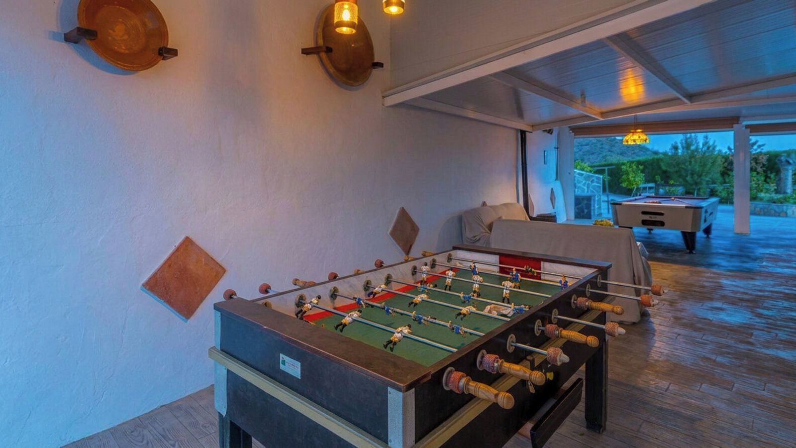 A foosball table in a room with a pool table and a covered outdoor area.