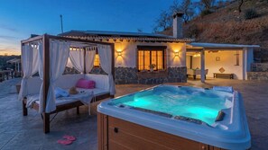 A hot tub with a wooden enclosure, a canopy bed with white curtains, and a stone building with a stone facade. - Cortijo La Envarra El Borge by Ruralidays (Málaga)