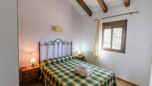Une chambre à coucher avec une couvre-lit à carreaux, une lampe de chevet, une table de nuit, une fenêtre avec des rideaux et un radiateur.