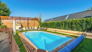 A rectangular swimming pool with a wooden deck, surrounded by a fence and a hedge.
