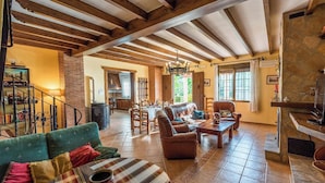 A spacious living area with a fireplace, wooden beams, a dining table, and comfortable seating.