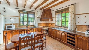 A kitchen with wooden cabinets, a central island, a microwave, and a large window. - Los Frailecillos Villanueva del Trabuco by Ruralidays (Málaga)