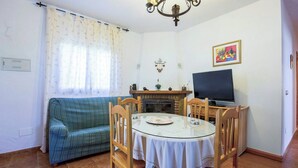 Ein Wohnzimmer mit einer Couch, einem Esstisch mit Stühlen, einem Kamin, einem Fernseher und einem Fenster mit Vorhängen.
