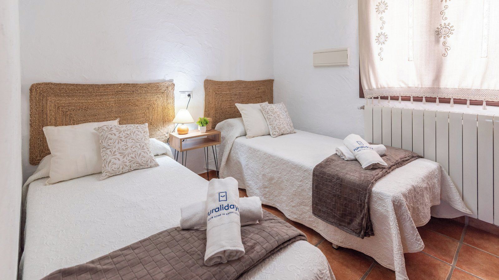 Hotellihuone, jossa on kaksi erillistä sänkyä, pieni yöpöytä lampun kanssa ja patteri.