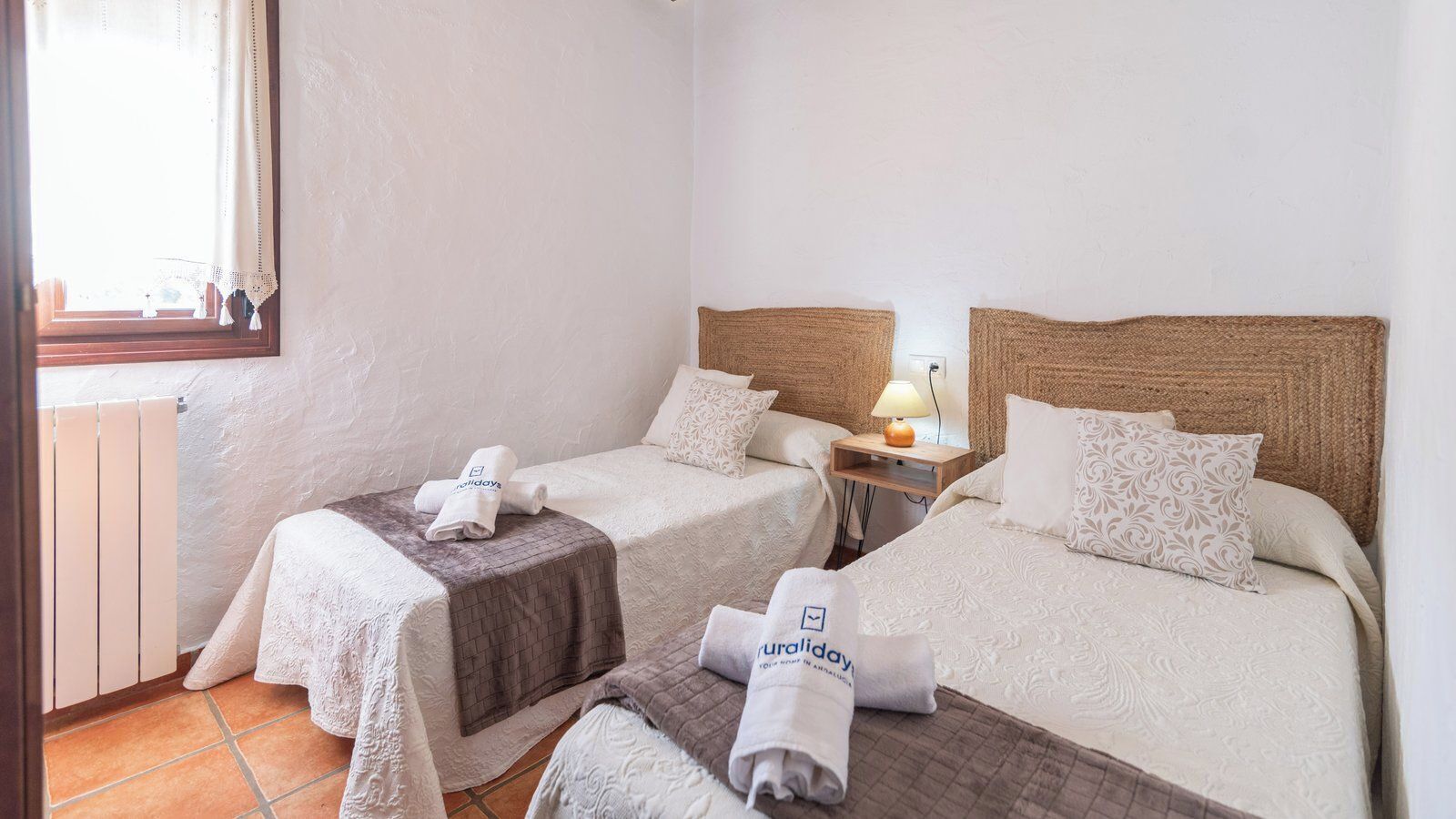 Une chambre d’hôtel avec deux lits, une petite table avec une lampe et une fenêtre avec un rideau.