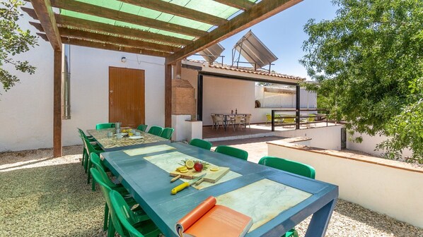 An outdoor patio with a long table set for dining, surrounded by green chairs.
